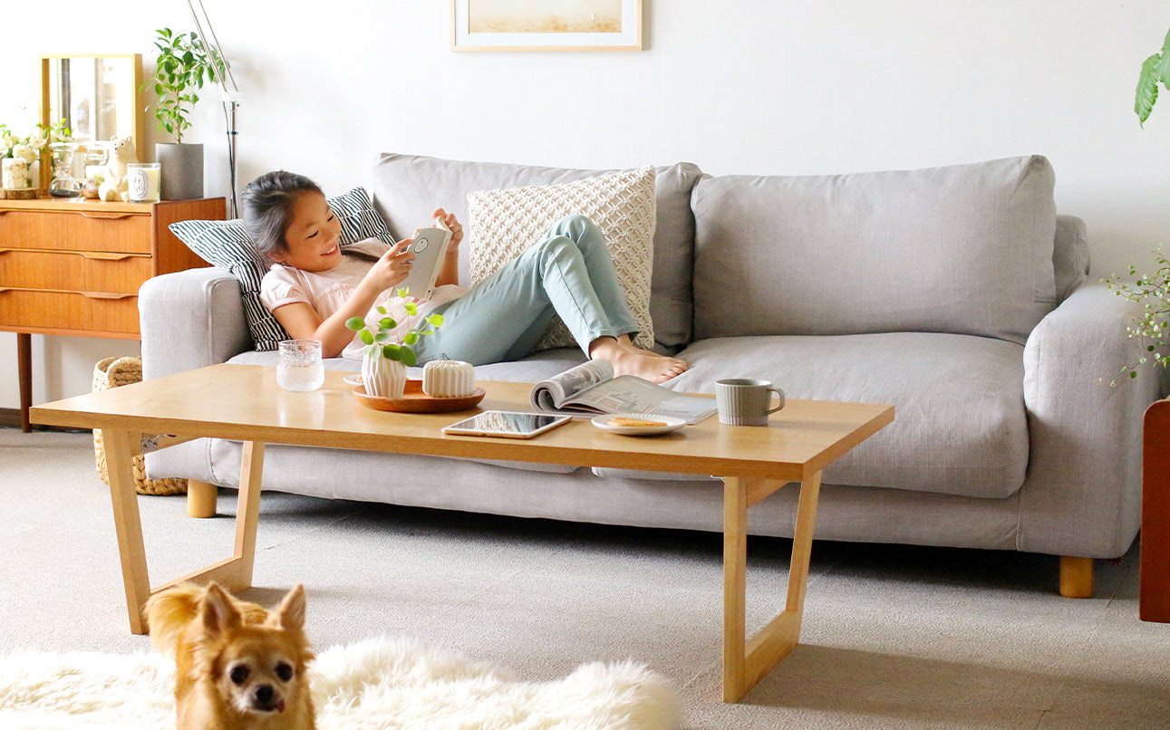 A young girl reading a book on Muji Wide Arm sofa covered in a Textured Weave Ash slipcover in a Japanese style living room