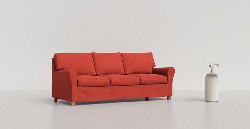 A red Angby sofa on a light grey background with a white vase beside it