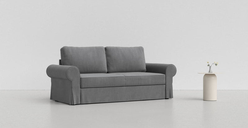 A medium grey IKEA Backabro sofa on a lighter grey background with a white vase beside it