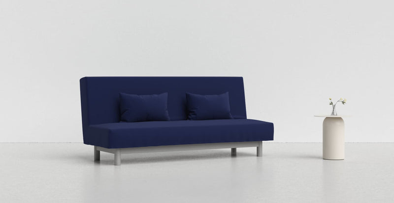 A dark blue Beddinge sofa on a light grey background with a white vase beside it