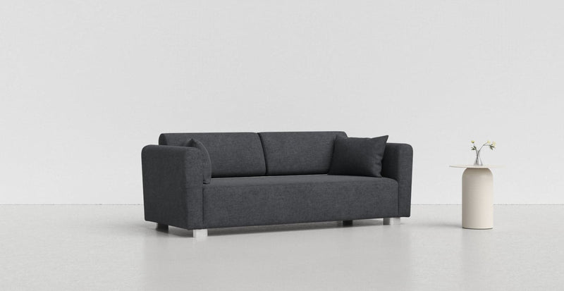 A charcoal grey Mysinge sofa on a light grey background with a white vase beside it