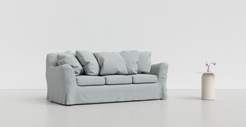 A cool grey Tomelilla sofa on a light grey background with a white vase beside it