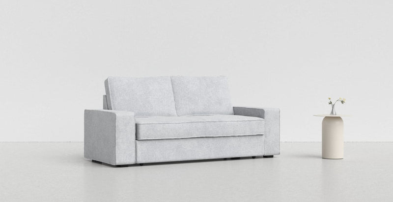 A light grey Vilasund sofa on a light grey background with a white vase beside it