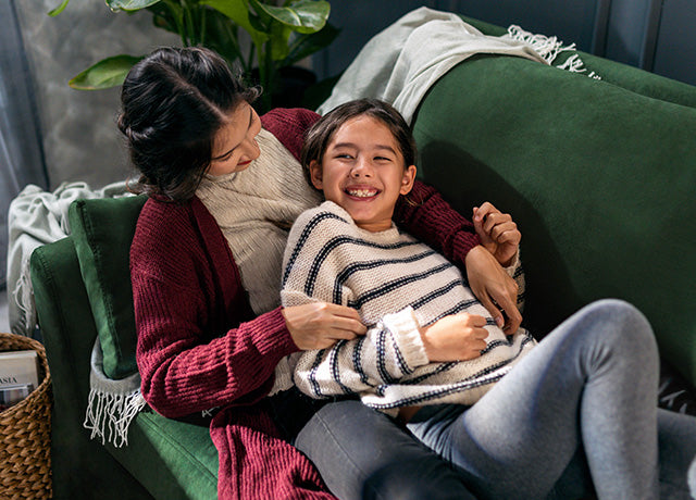 Mother and daughter cuddling on IKEA FARLOV three-seater sofa with Classic Velvet Forest Green slipcover