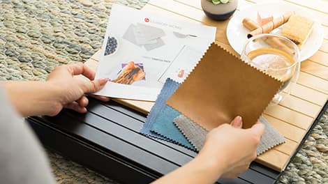 Woman holding an array of fabric sample swatches and a sample booklet, placed on an armrest tray