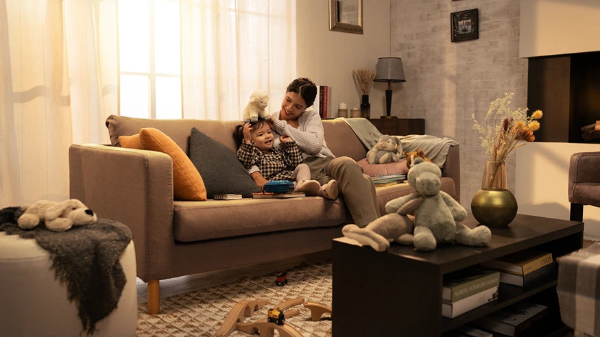 A heartwarming scene of a mother and child playing on a cozy living room sofa, featuring a neutral-toned sofa that could benefit from protective slipcovers or covers, enhancing its longevity and style. This comfortable couch is adorned with pillows and surrounded by toys, creating a perfect family space.