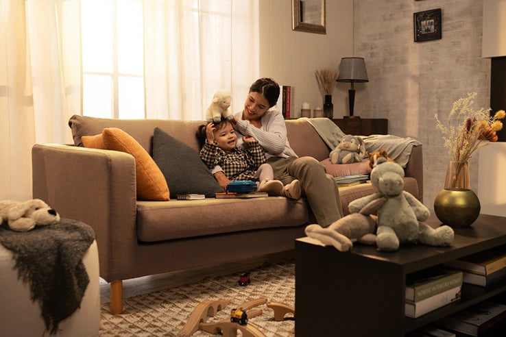 
A heartwarming scene of a mother and child playing on a cozy living room sofa, featuring a neutral-toned sofa that could benefit from protective slipcovers or covers, enhancing its longevity and style. This comfortable couch is adorned with pillows and surrounded by toys, creating a perfect family space.