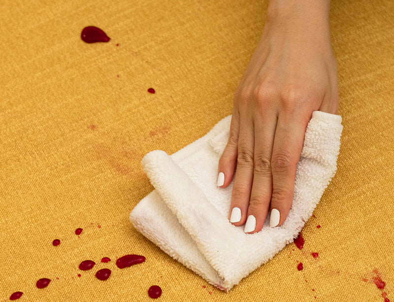 A hand diligently cleaning up a spilled liquid on a sofa with a spill-proof Performance Weave Amber slipcover