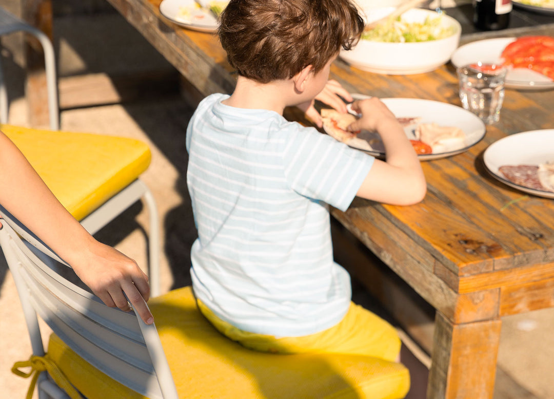 Kid sitting on a chair cushion with Performance Tweed Amber slipcover outdoors, enjoying a meal
