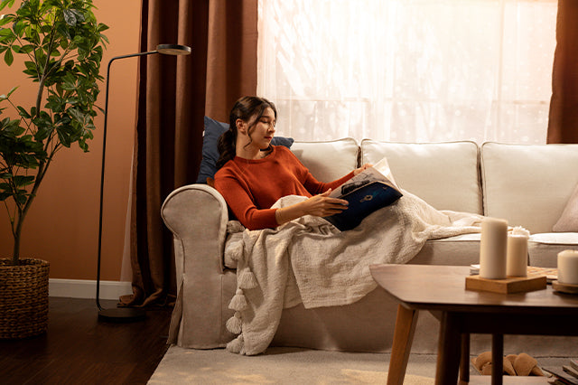 Cosy living room with a woman relaxing on a beige sofa slipcover from Comfort Works, featuring custom couch covers for a warm and inviting space