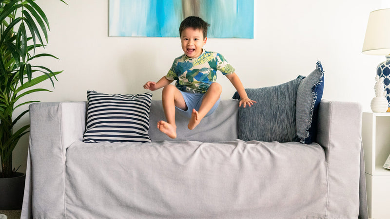 Kid jumping on grey IKEA KLIPPAN sofa with Everyday Weave Pebble slipcover