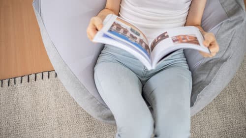 A girl sitting on a grey Muji Beads sofa while reading a magazine (Alternate angle)